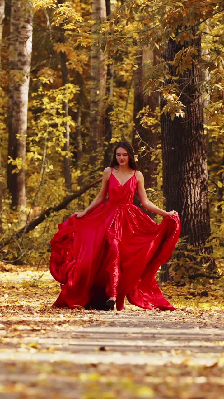 Una Bella Donna in un Abito Rosso Fluente Immortalata in una Incantevole Foresta Autunnale, Circondata da Foglie Dorate e un Sentiero Sereno nell'Abbraccio della Natura