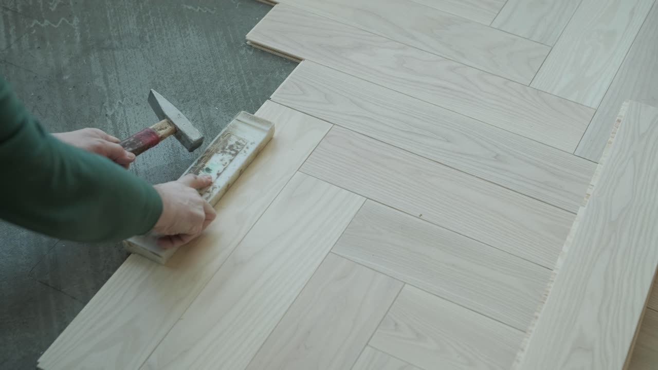Worker installing wooden flooring with hammer and tapping block