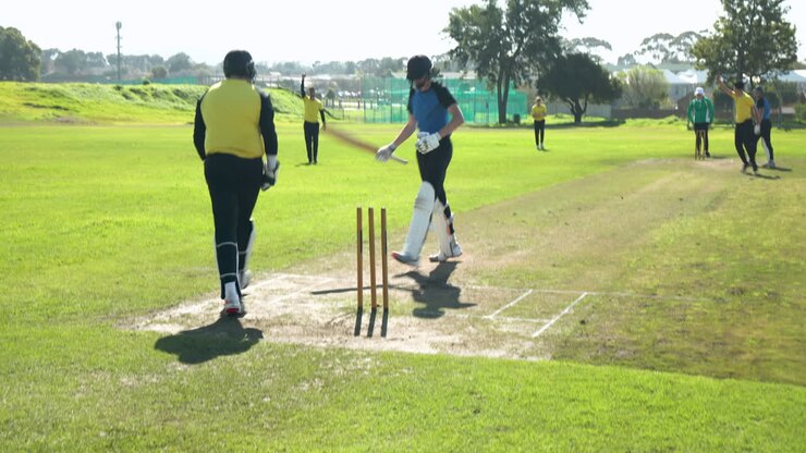 Giocatori di cricket che camminano sul campo in una giornata di sole, preparandosi per la partita.