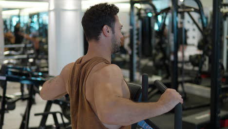 sporty man training back and shoulder muscles in seated row machine in modern gym