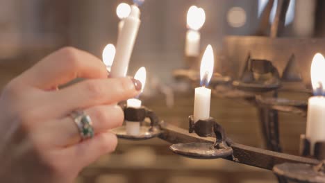 la mano de una persona encendiendo una vela en un candelabro votivo - vela de oración