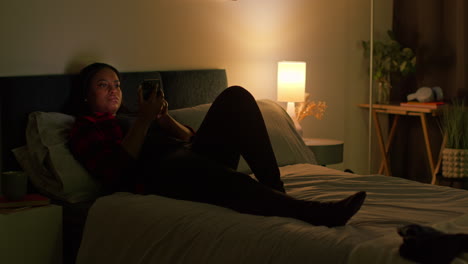 woman using phone in bed at night