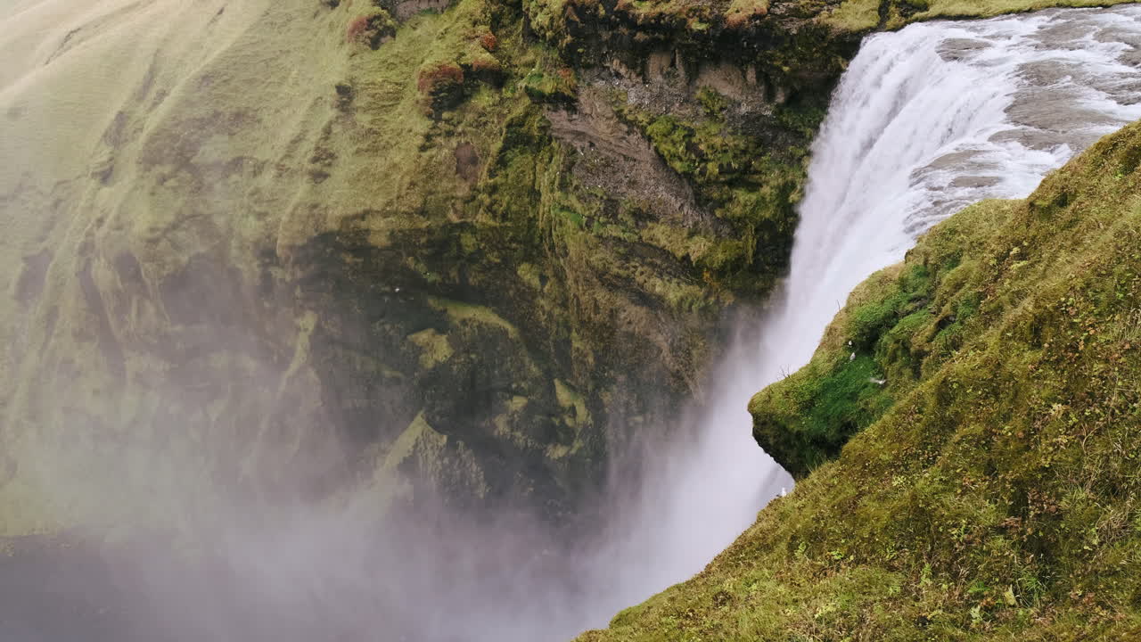 el agua poderosa se vierte sobre un acantilado cubierto de musgo en la parte superior de la cascada skogafoss, islandia