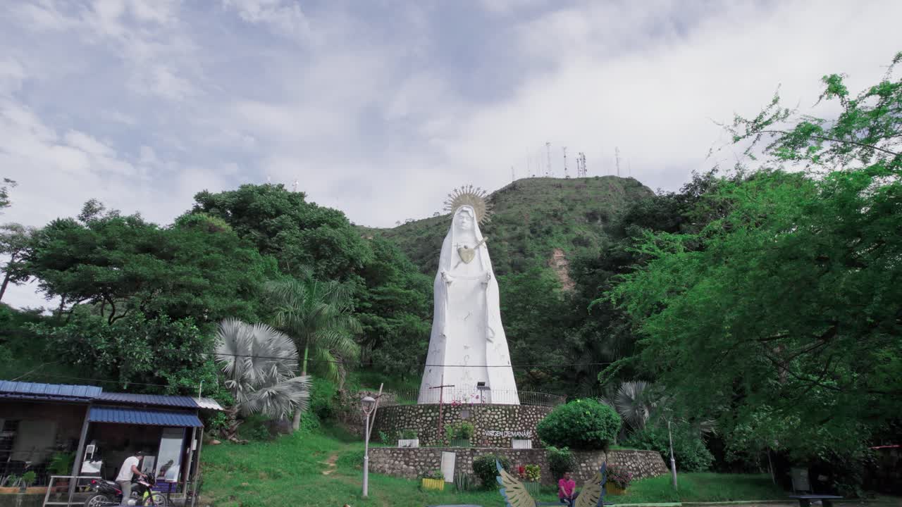 Drone zoom out showing the Virgen de Manare statue surrounded by lush vegetation in Yopal, Colombia, on a bright day