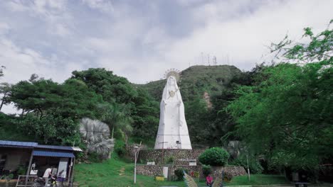 drone zoom out showing the virgen de manare statue surrounded by lush vegetation in yopal, colombia, on a bright day
