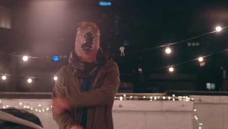 hombre gracioso con máscara de caballo bailando bajo la lluvia en el techo por la noche divirtiéndose realizando movimientos de baile tontos celebrando el fin de semana
