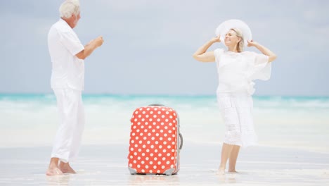 caucasian seniors on beach with camera and suitcase