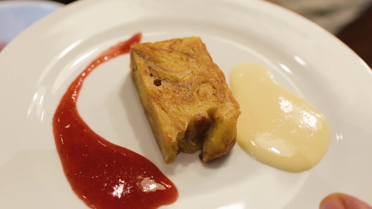 Un cucchiaio di metallo versa salsa rossa di fragole su un piatto bianco con budino di pane.