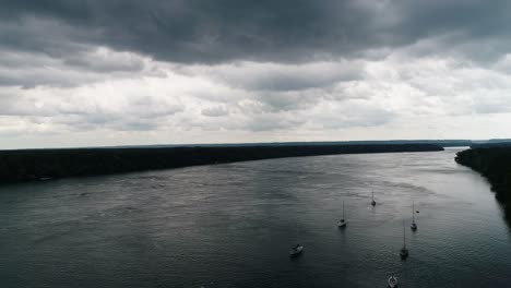 Ariel-drone-captures-a-still-lake-with-several-sailboats-and-a-dock-and-marina,-outlined-by-dark-trees