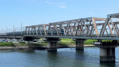 a train crosses a steel bridge over a calm river on a clear day