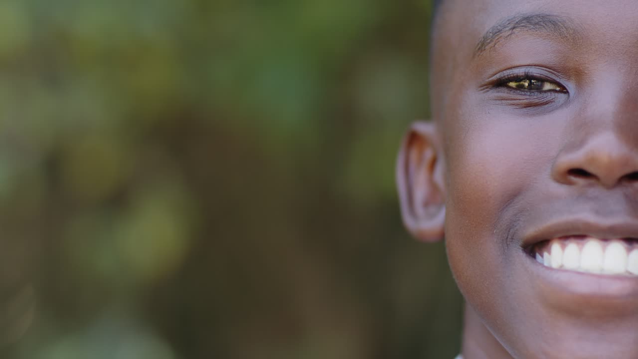 African youth male moving neutral face into laughter before blurred leaves shirt collar, copy space