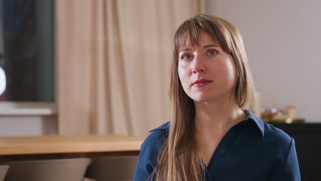 portrait of therapist seated on green sofa in cozy modern office, long hair, blue blouse, attentive eyes lit by soft evening light through window, offering guidance and support to patient in session