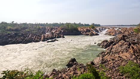 dynamic view of khone phapheng falls with powerful water flow, rocky terrain, and lush greenery under bright daylight