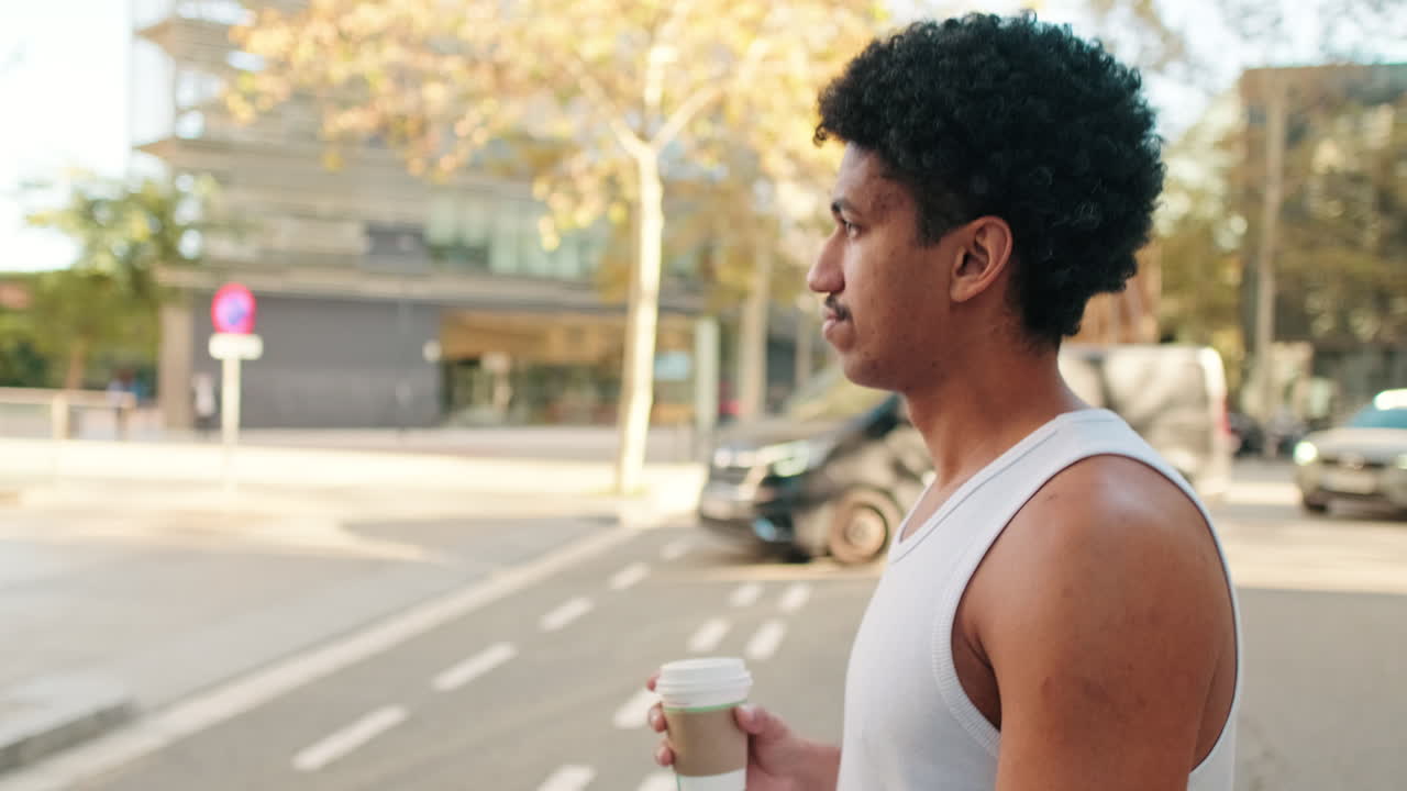 Giovane uomo con capelli ricci che tiene in mano una tazza di caffè per strada in città