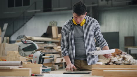 carpenter working with blueprints and digital tablet in a workshop
