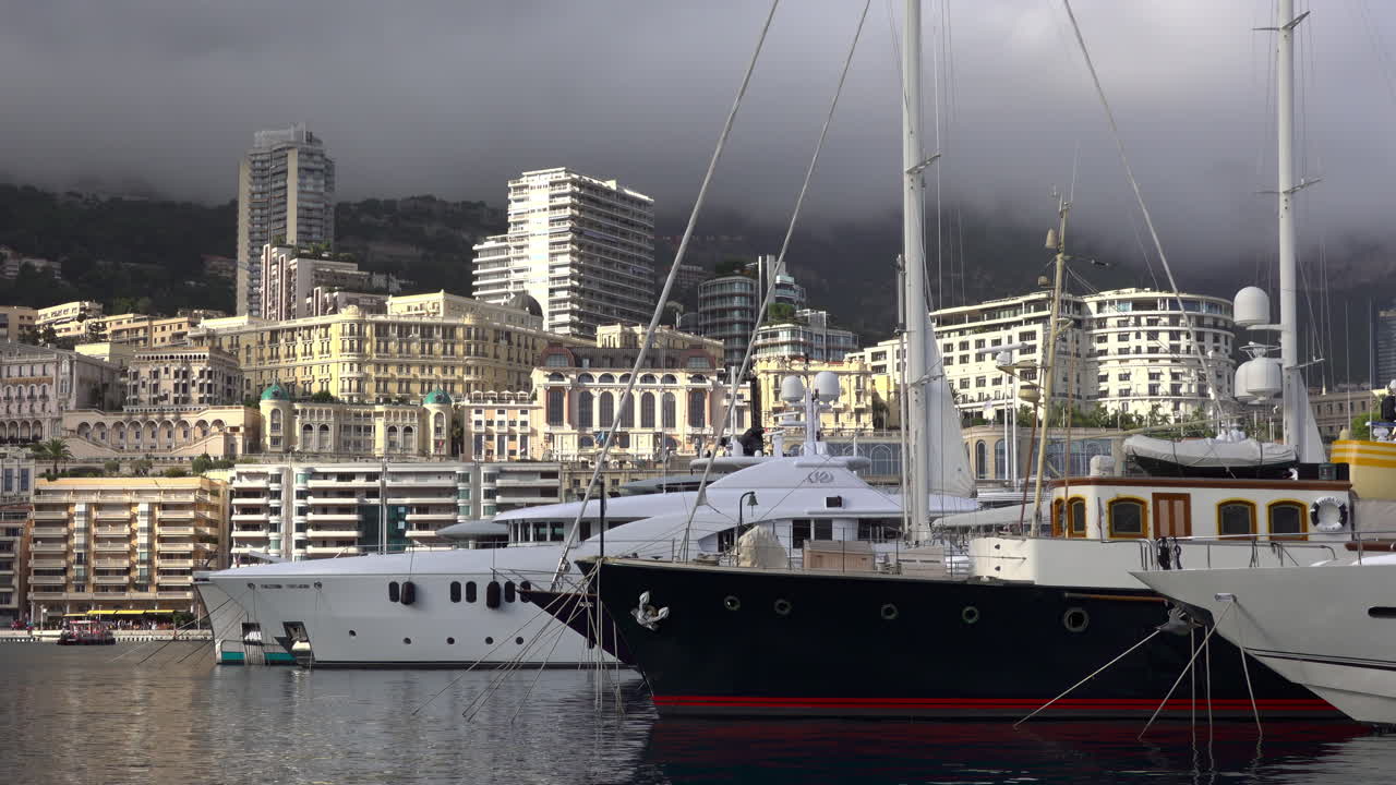 La Condamine, Monaco - July 4, 2025: Row of sleek luxury yachts, docked in Port Hercules with the Monaco cityscape and misty hills in the background