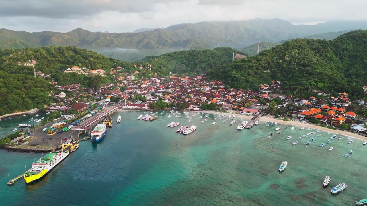 Tropikal tepeler ve korunaklı koy suları ile çevrili hareketli bir sahil kasabasının yanında yolcu feribotları ve balıkçı tekneleriyle dolu liman, yukarı eğilerek ortaya çıkaran drone çekimi.