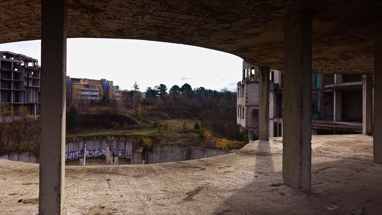 L'esplorazione urbana rivela la bellezza spettrale di una struttura abbandonata a più livelli tra cieli nuvolosi e paesaggi selvaggi