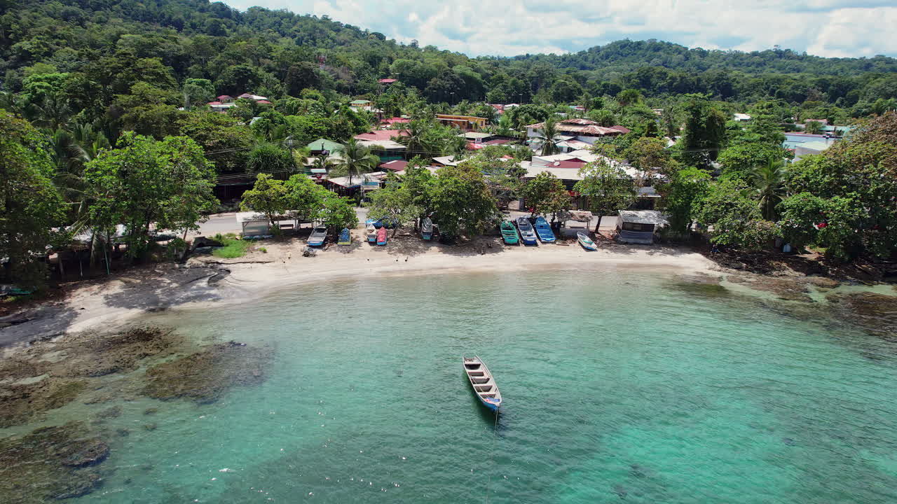 Aerial shot of a lush, scenic beach with fishing boats by the turquoise shallow water in the port town of Puerto Viejo, a vibrant tourist destination on the Caribbean coast of Costa Rica.