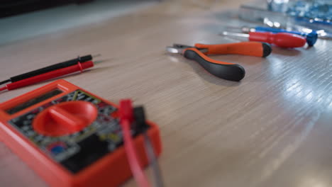 a close-up view of a workbench featuring various electronic tools, including a red multimeter, pliers, screwdrivers, and probes