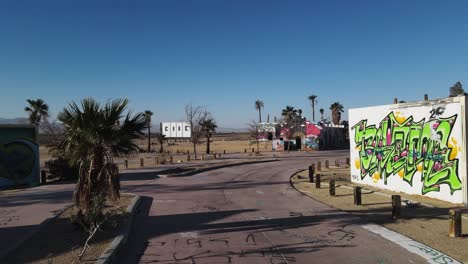 Luftaufnahmen-Von-Sich-Nähernden-Gruseligen-Verlassenen-Gebäuden-Mit-Farbenfrohen-Graffiti-In-Der-Kalifornischen-Mojave-Wüste