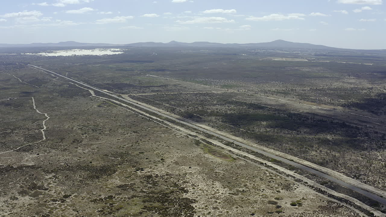 vista aérea de una carretera pavimentada que atraviesa un paisaje seco y árido con montañas en la distancia.