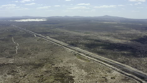 aerial view of a paved highway traversing a dry, arid landscape with mountains in the distance.