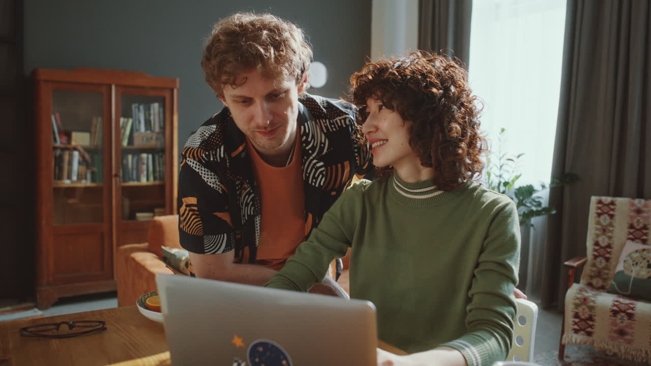 Smiling Couple Looking at Laptop Screen and Talking in Living Room