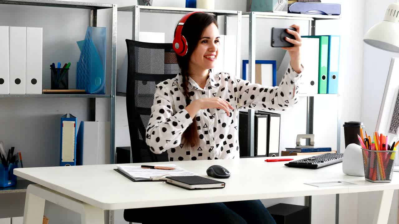 mujer de negocios con auriculares rojos grabando video en un teléfono inteligente en una oficina moderna