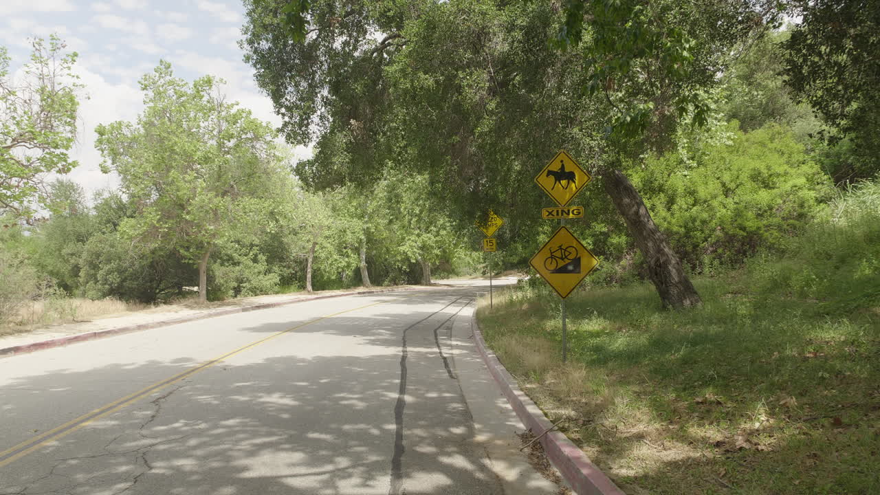Filmato DSLR 4K a 10 bit dettagliato diurno catturato a Griffith Park che mostra un segnale di attraversamento cavalli accanto a un segnale di pericolo che avverte i ciclisti in discesa