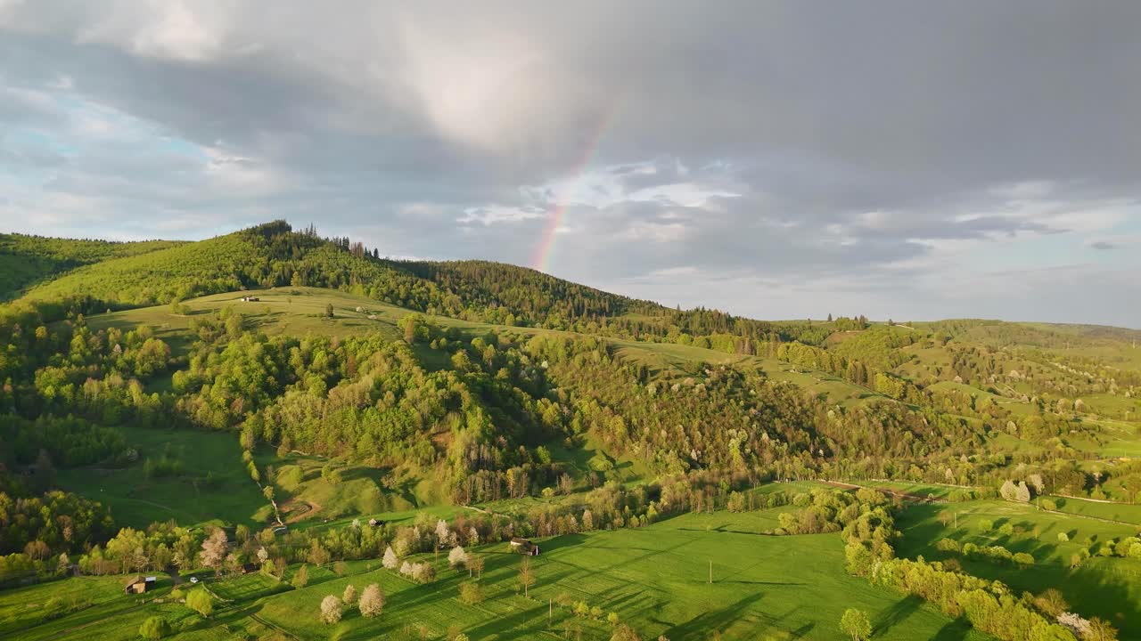 Drone video of forested hills between Poiana Micului and Manastirea Humorului, Romania, at sunset with a rainbow