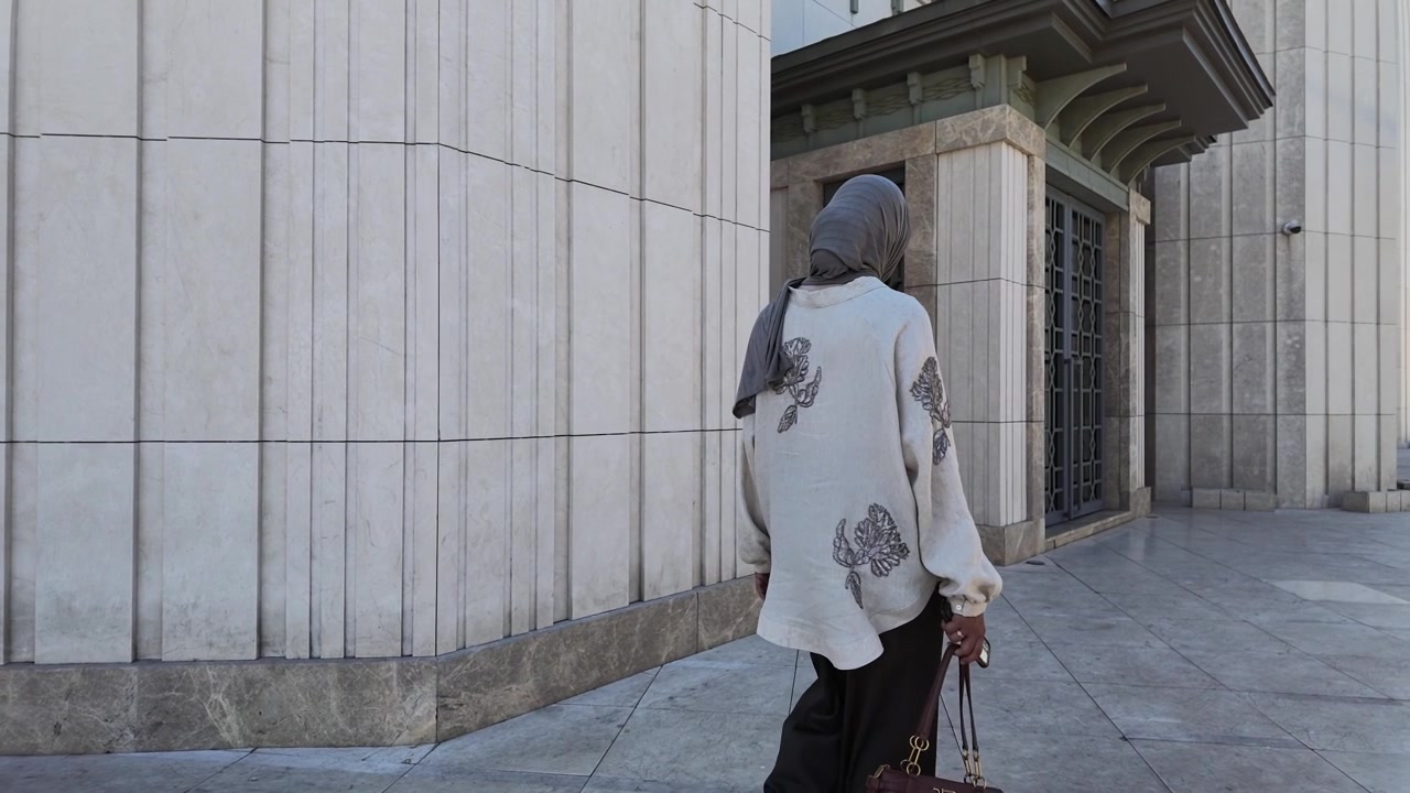 Donna con hijab che cammina davanti a un moderno edificio in pietra