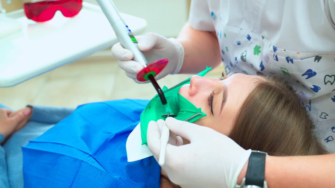 Treatment and filling of a tooth with a photopolymer lamp. The girl at the dentist in white gloves