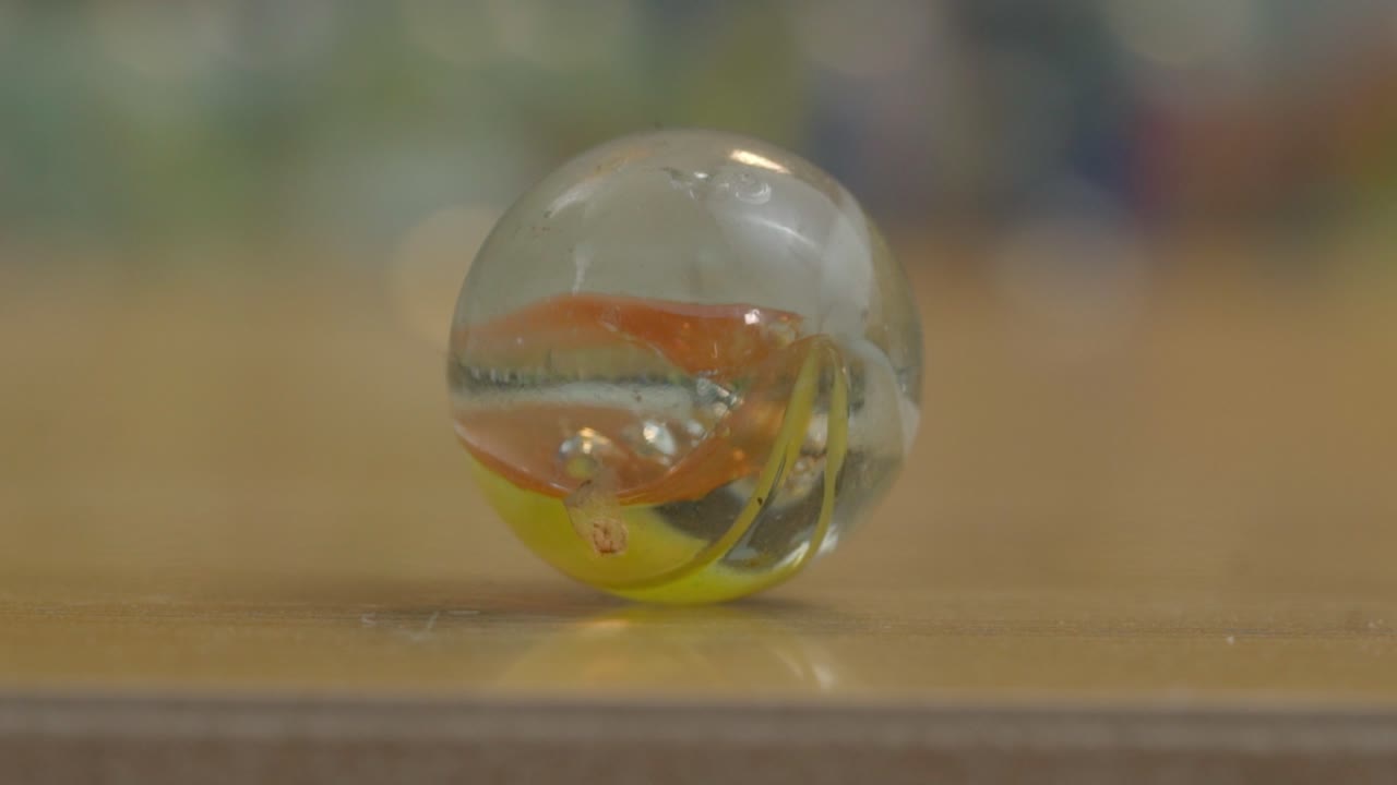 Close up of a colorful glass marble resting on a wooden surface with shallow depth of field