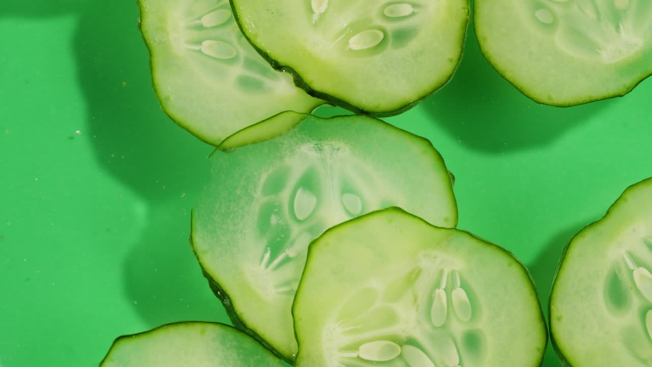 Cucumber slices rotate in splashes of juice on white background. High quality 4k footage