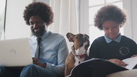 father and son sitting on the sofa at home working with their pet dog sitting between them, low angle, close up