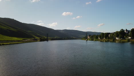 Vuelo-Sobre-El-Lago-Mosel-Hacia-Un-Puente-Junto-A-Un-Pueblo-Y-Un-Viñedo