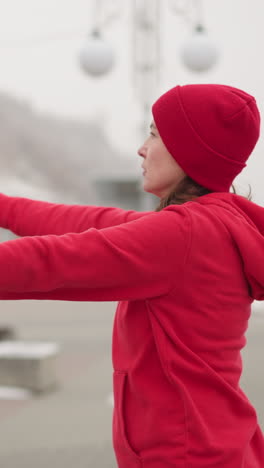vista trasera de una mujer estirando los brazos al aire libre en un entorno de invierno con personas borrosas y postes de luz en el fondo, mostrando una rutina de entrenamiento serena en un entorno urbano rodeado de ligera nevada