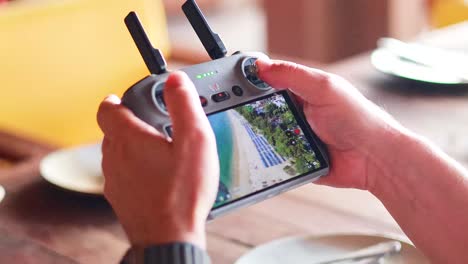 hands operate a drone controller displaying aerial views of phuket, thailand. bright indoor lighting highlights the device and screen