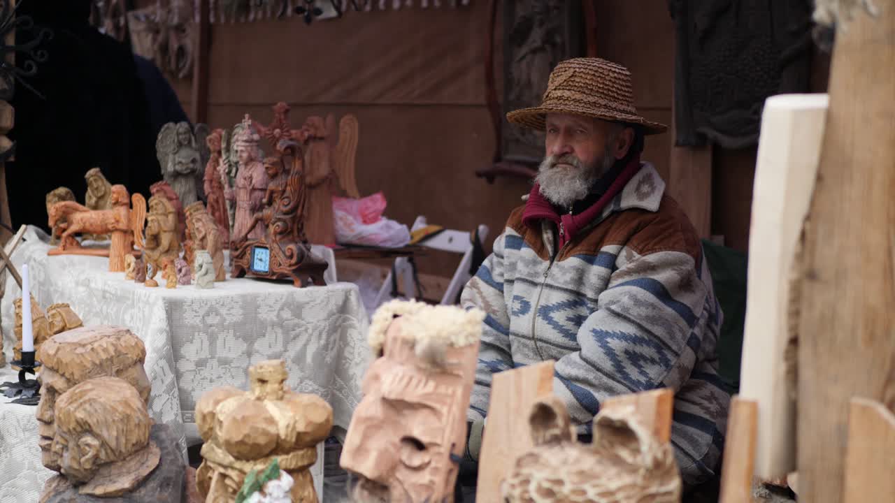 Handsome old man sitting outside and selling his own wood carvings. Senior with gray beard.