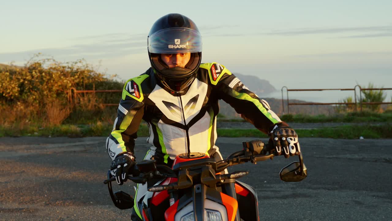 Motorcyclist in gear on sport bike on scenic roadside during sunset with a distant view