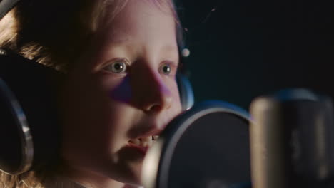 la niña practica la voz en el micrófono de cerca. el niño talentoso demuestra habilidades vocales en el estudio de grabación. el niño dotado canta una canción en el studio de audio