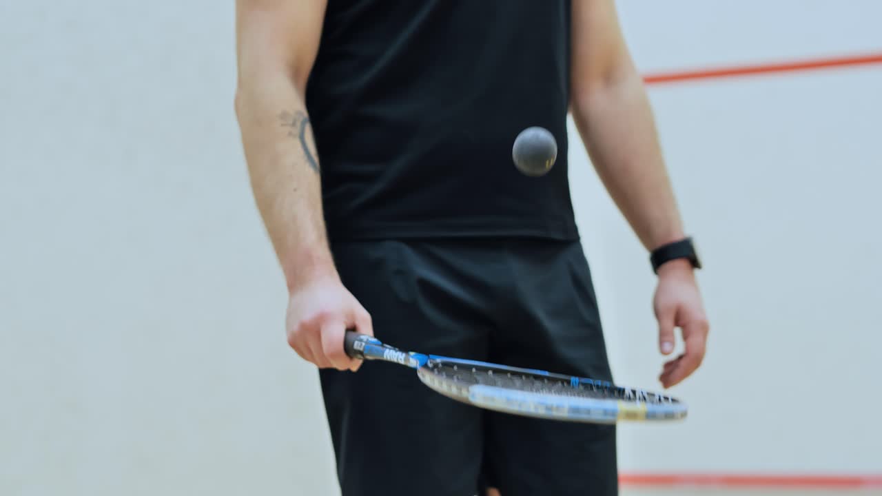 Focused male athlete balancing squash ball on racket before competitive match