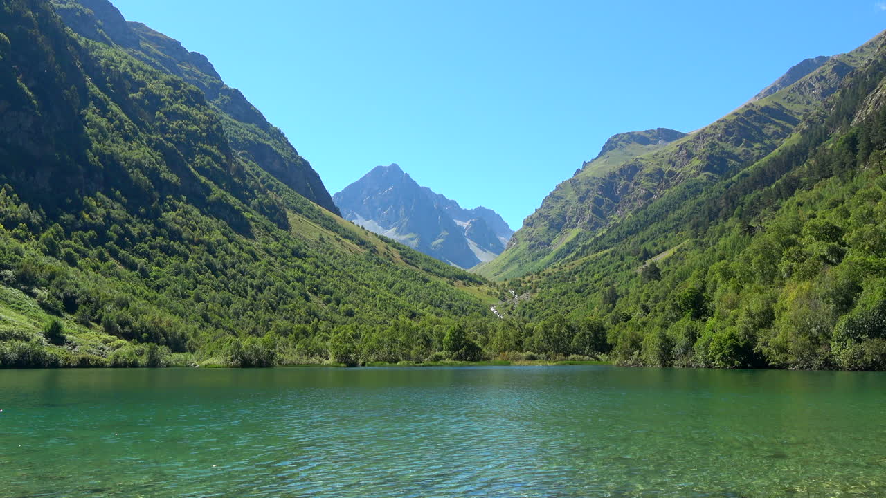 Ampla vista panorâmica de um lago de montanha tranquilo, rodeado por encostas verdes arborizadas e picos altos, perto de Dombay, Cáucaso, Rússia, em um dia de verão claro e ensolarado.