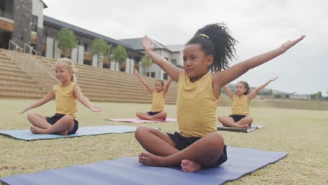 video de niñas diversas enfocadas practicando yoga en esteras frente a la escuela