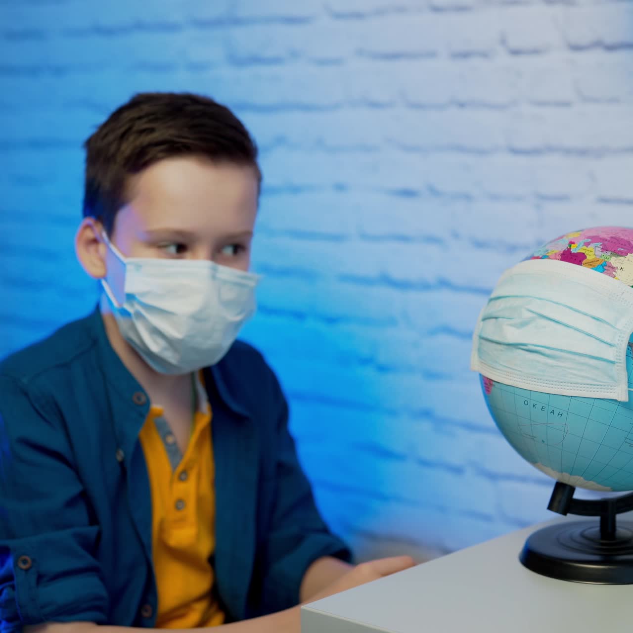 Boy looking at globe learning about virus spreading around the world. Child with curious face thinking about the planet during covid lock down. Concept of COVID-19 pandemic infection.