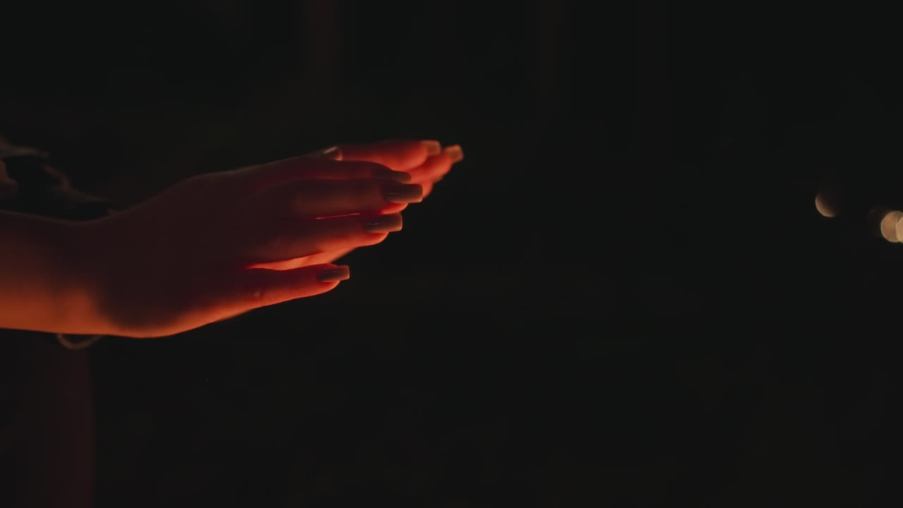 담요를 입은 여자가 불 위에 손을 들고, 젊은 여자가 추운 늦은 밤 동안 손을 따뜻하게하려고 노력합니다.