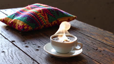 Hot Coffee with Steam and Colorful Pillow on Wooden Table