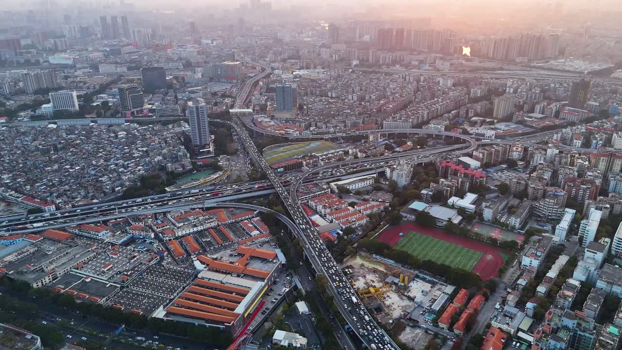 Aerial view of Guangzhou during sunset, showing busy rush hour traffic on the highways. The cityscape features a mix of urban sprawl, roads, and residential buildings. China