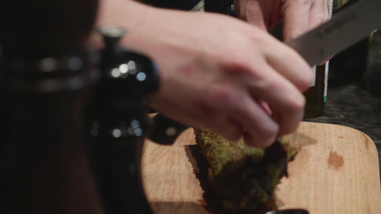 Lo chef taglia costolette di cervo speziate su un tagliere di legno, dopo la cottura in forno